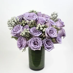 Elegant lavender rose arrangement accented with silvery brunia berries in a modern glass vase wrapped with deep green leaves, photographed against a white backdrop — Reykjavik Twilight by Athletic Club Flower Shop.