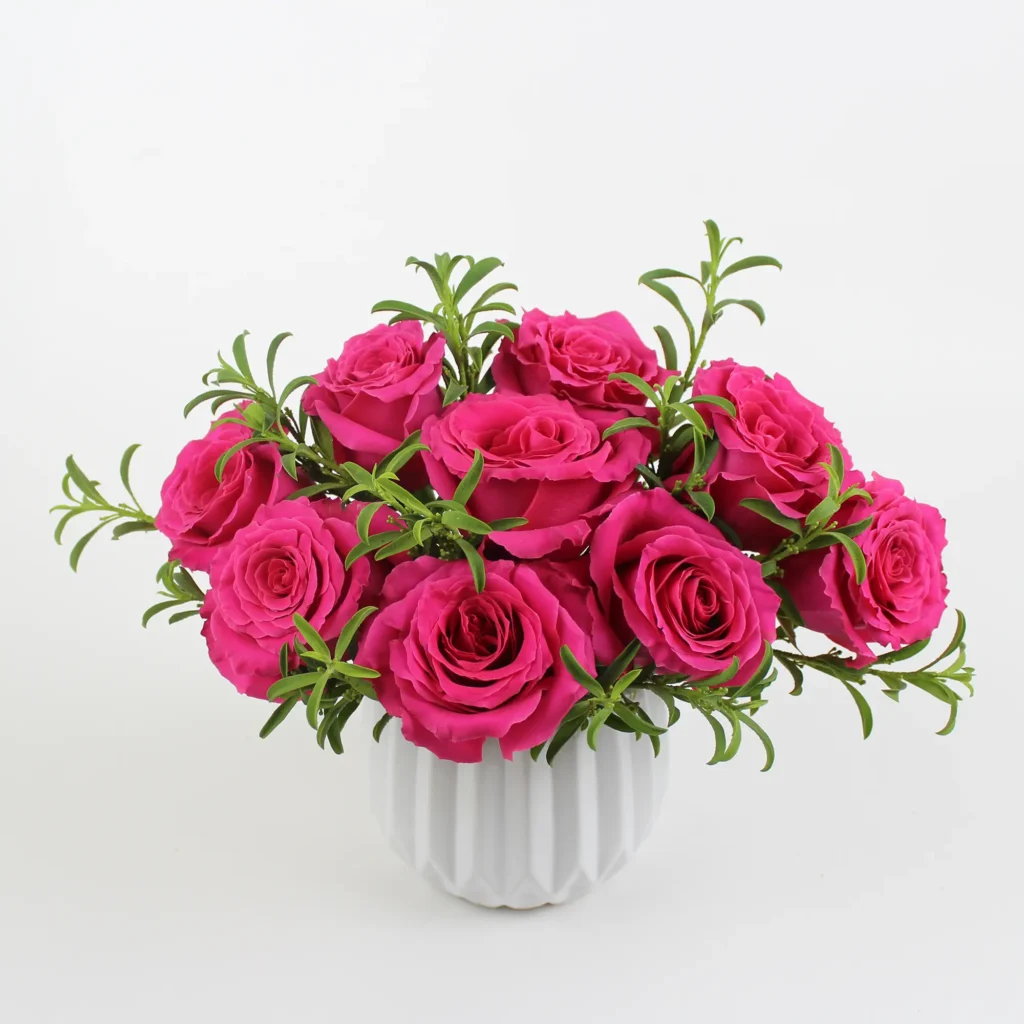 Hot pink rose bouquet with fresh green foliage arranged in a modern white ceramic vase, displayed against a white background. Miami Heatwave floral arrangement by Athletic Club Flower Shop.